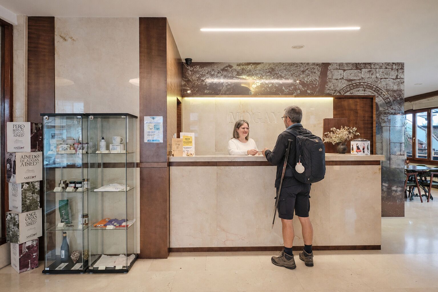 A reception desk with a woman behind it, a man standing in front, and a glass display case to the left.