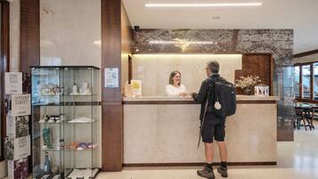 A reception desk with a woman behind it, a man standing in front, and a glass display case to the left.