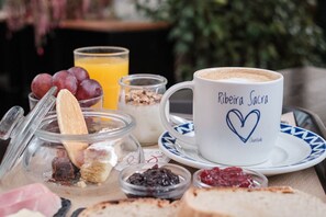 A breakfast setting with a cup labeled 'Ribeira Sacra,' a glass of orange juice, and various food items like bread, jam, and yogurt. - Hotel Mogay (Chantada)