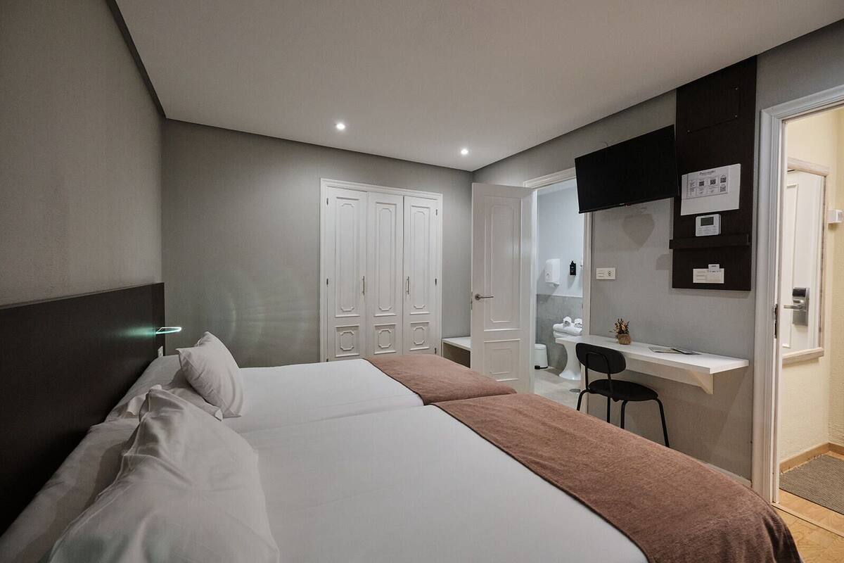 A hotel room with a bed, a desk, a chair, and a bathroom visible through an open door.