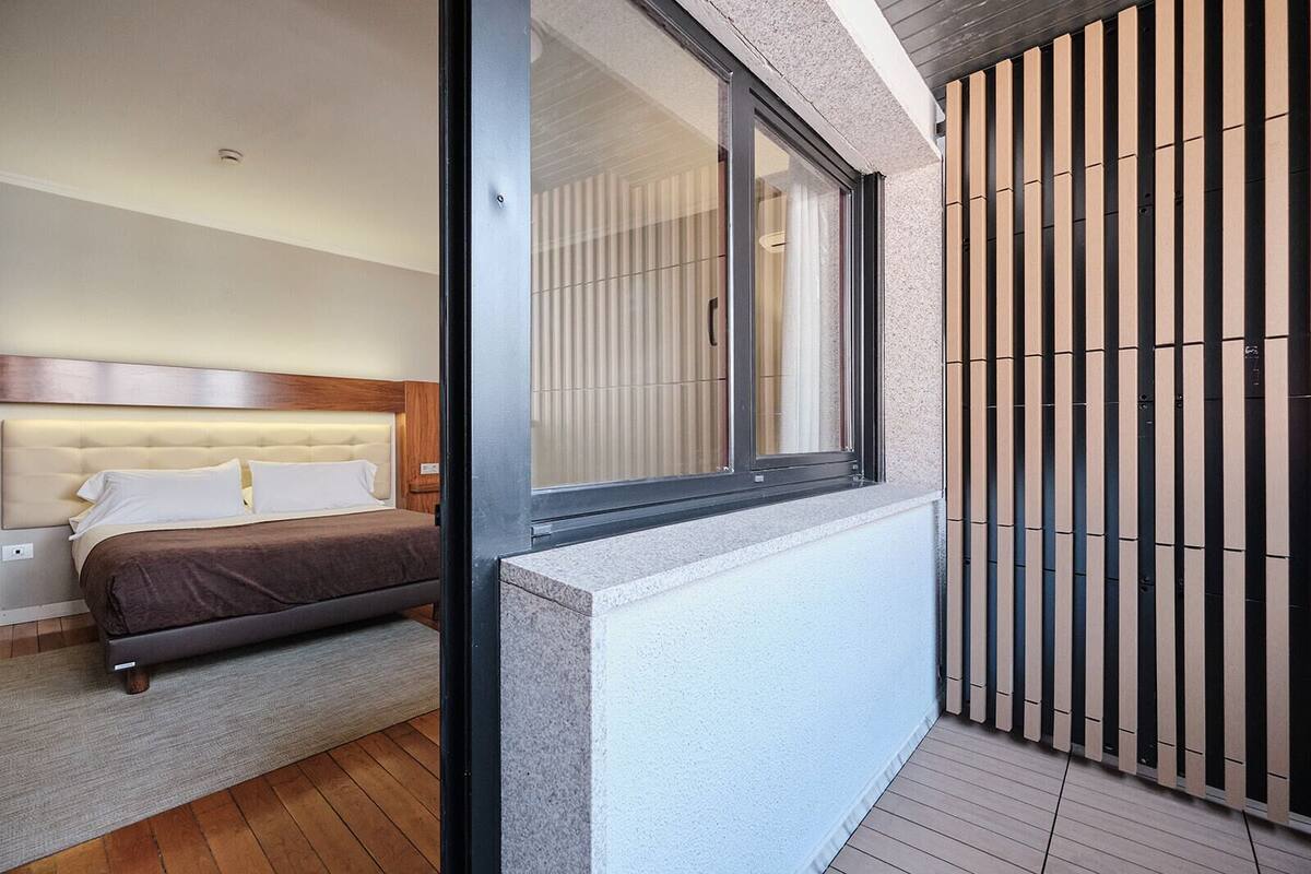 A bedroom with a bed, a window, and a view of a wooden fence.