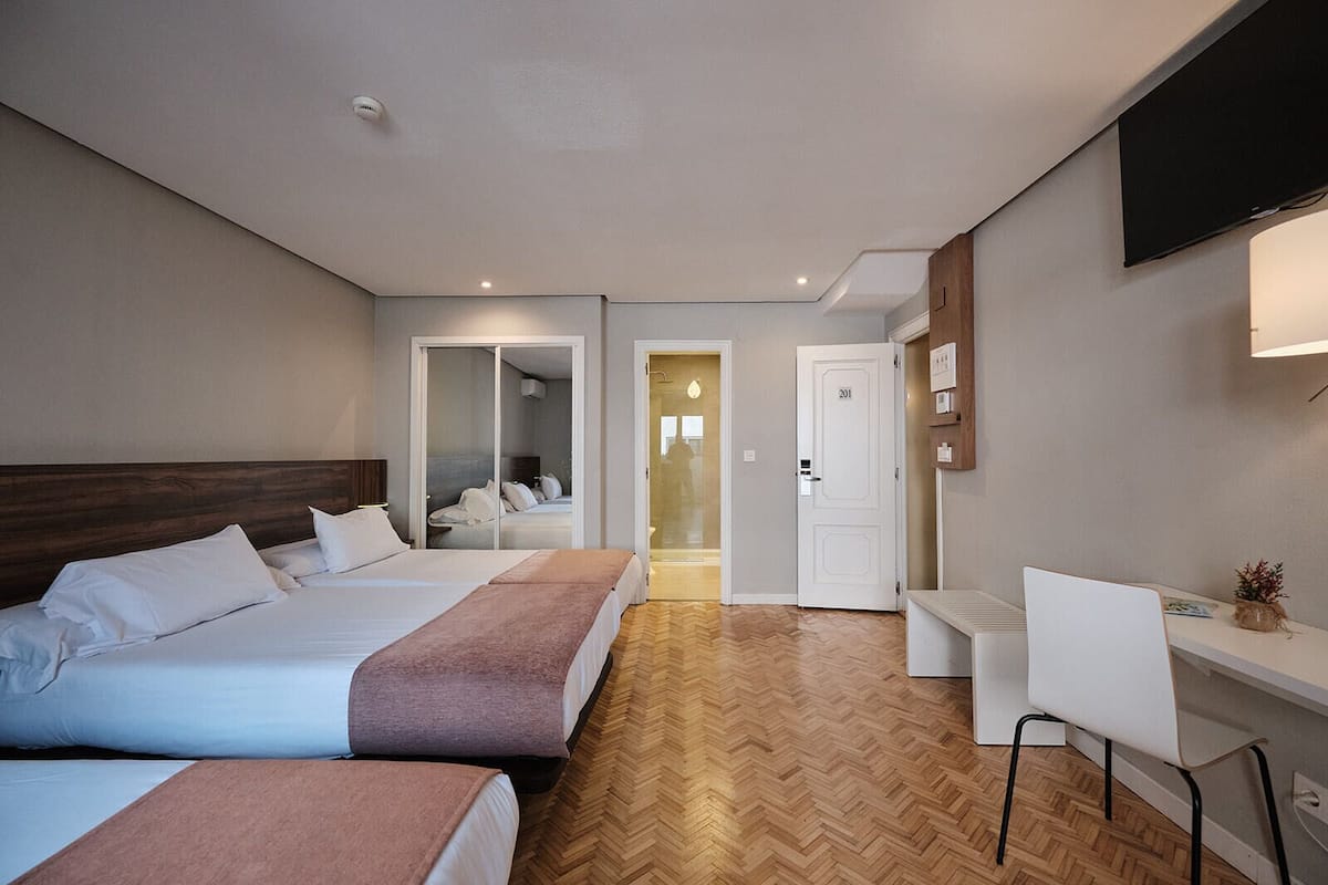 A hotel room with two beds, a desk, a chair, a TV, and a mirror.