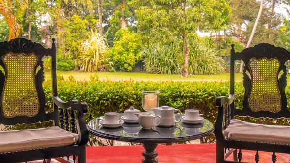 A round table with a glass top, surrounded by two chairs with intricate back designs. The table is set with white teacups, a teapot, and a candle in a glass holder. - EKHO Weligama (Weligama)