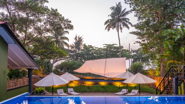 A swimming pool with lounge chairs and umbrellas, surrounded by lush greenery and palm trees. - EKHO Weligama (Weligama)