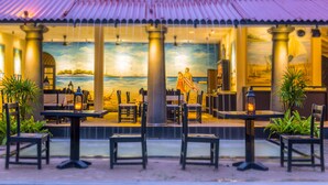An outdoor dining area with tables and chairs, a mural of a beach scene, and a view of the ocean. - EKHO Weligama (Weligama)