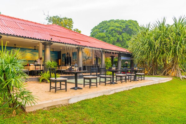 An outdoor restaurant with tables and chairs, a red roof, and greenery around. - EKHO Weligama (Weligama)