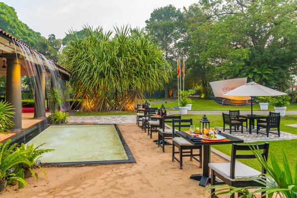 An outdoor dining area with tables and chairs, a water feature, and lush greenery. - EKHO Weligama (Weligama)