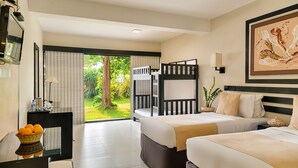 A hotel room with two beds, a desk with a basket of oranges, a TV, and a large window with a view of greenery. - EKHO Weligama (Weligama)
