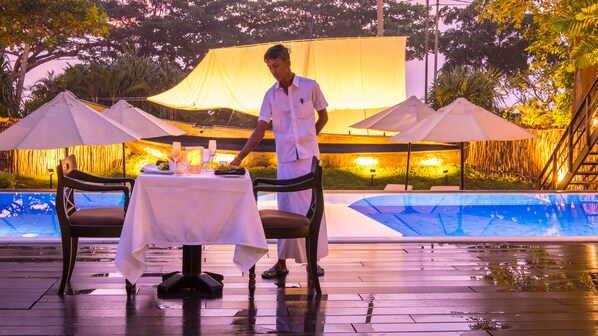 A dining area with a table set for two, a pool, and outdoor umbrellas. - EKHO Weligama (Weligama)