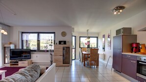 A modern living room with a TV, sofa, and dining area. - Ferienwohnung Seeblick (Schalkenmehren)