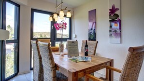 A dining area with a wooden table, wicker chairs, a vase with flowers, and a menu. - Ferienwohnung Seeblick (Schalkenmehren)