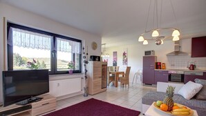 A modern living room with a TV, a dining area, and a kitchen. - Ferienwohnung Seeblick (Schalkenmehren)