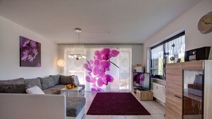 A modern living room with a sofa, a coffee table, a TV, and a large window with a view. - Ferienwohnung Seeblick (Schalkenmehren)