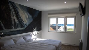 Une chambre avec deux lits, un grand tableau représentant une cascade, une fenêtre donnant sur la plage et un téléviseur fixé au mur.