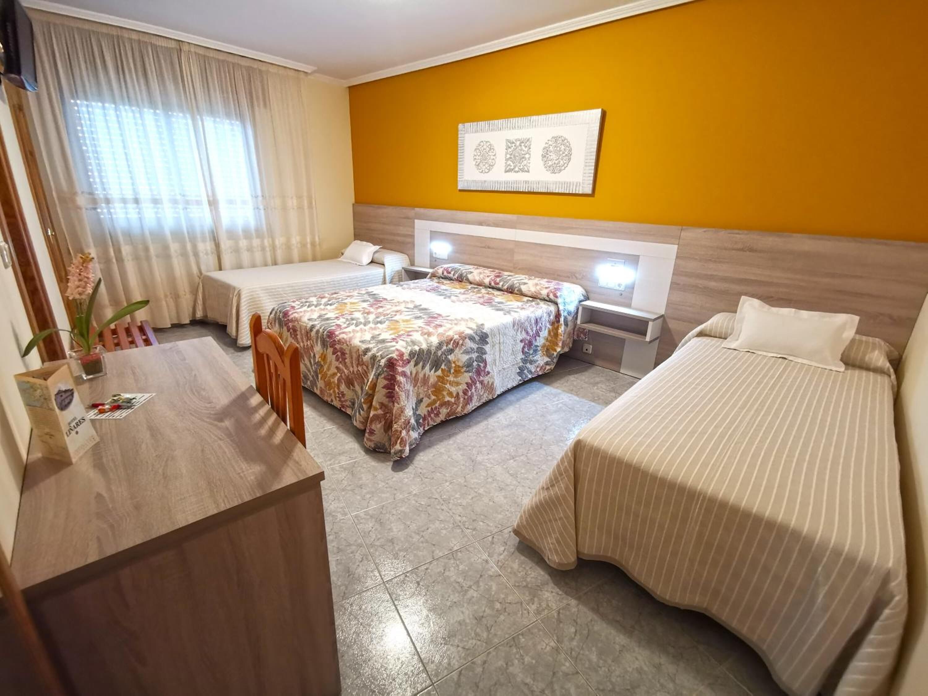 Een hotelkamer met twee bedden, een bureau en een stoel. Er is een raam met gordijnen, een kunstwerk aan de muur en een bloempot.