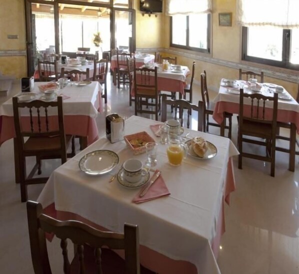 A dining area with multiple tables set for breakfast, featuring plates, cups, and a toaster.