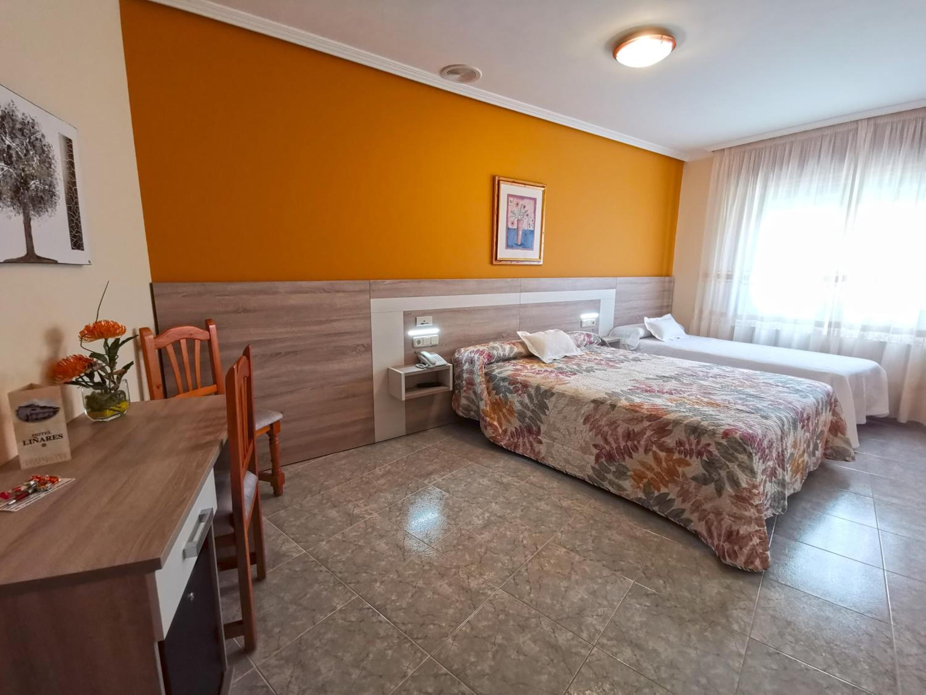 Une chambre d’hôtel avec deux lits, un bureau avec une chaise, un vase de fleurs et un tableau au mur.