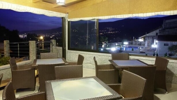 An outdoor seating area with wicker furniture and a view of a cityscape at night. - Hotel Liñares (Poio)