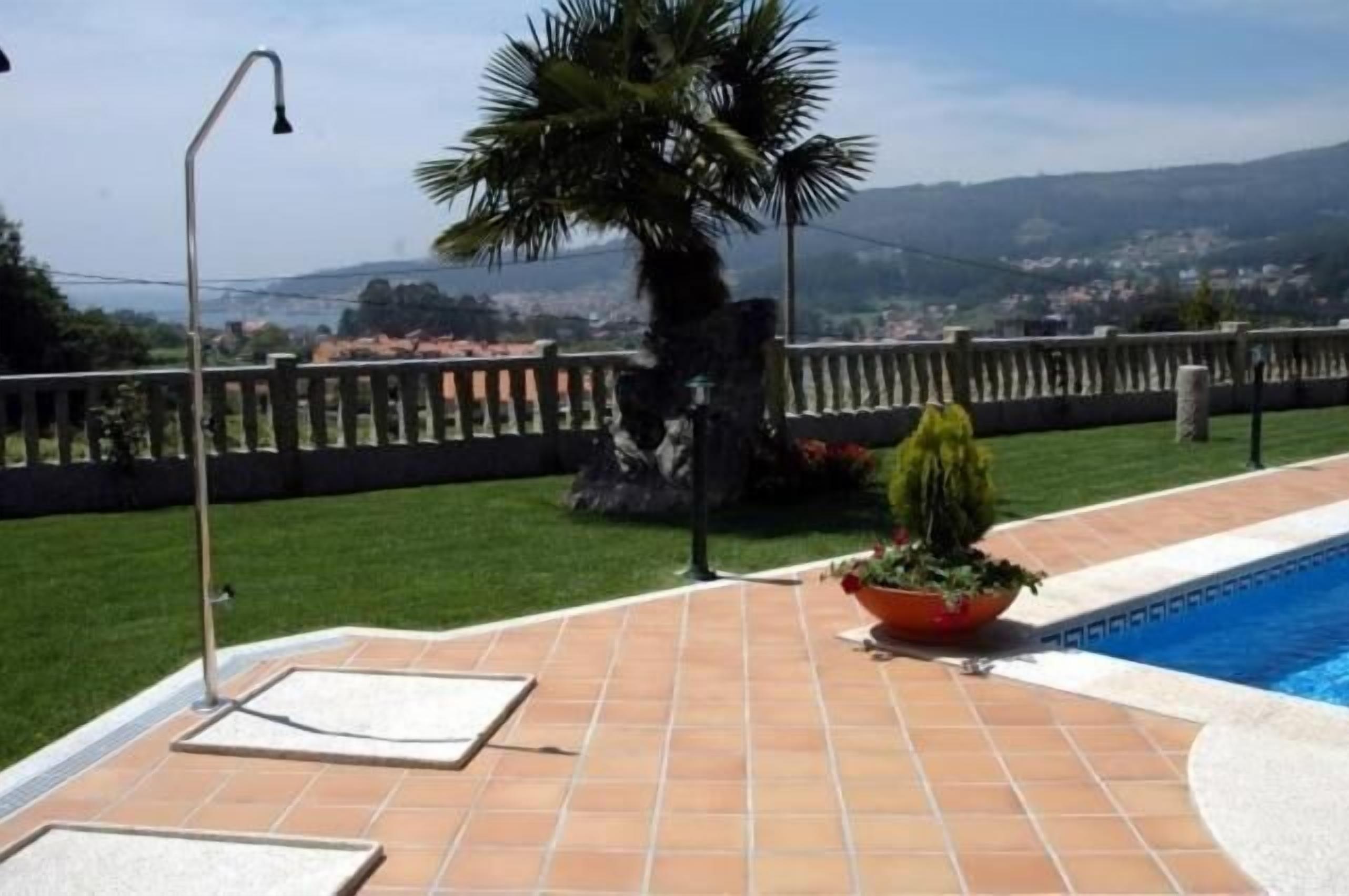Una piscina con borde de baldosas, una palmera y vista a un pueblo lejano.