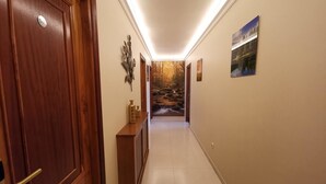 A hallway with a wooden door, a decorative wall piece, and a view of a scenic outdoor area through a glass door at the end. - Hotel Liñares (Poio)