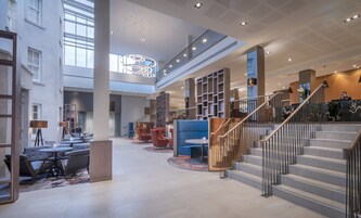 Un'ampia hall con una scalinata, zone relax e un soffitto alto illuminato con luci moderne.