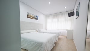 A hotel room with two beds, a flat-screen TV mounted on the wall, and a large window with sheer curtains.