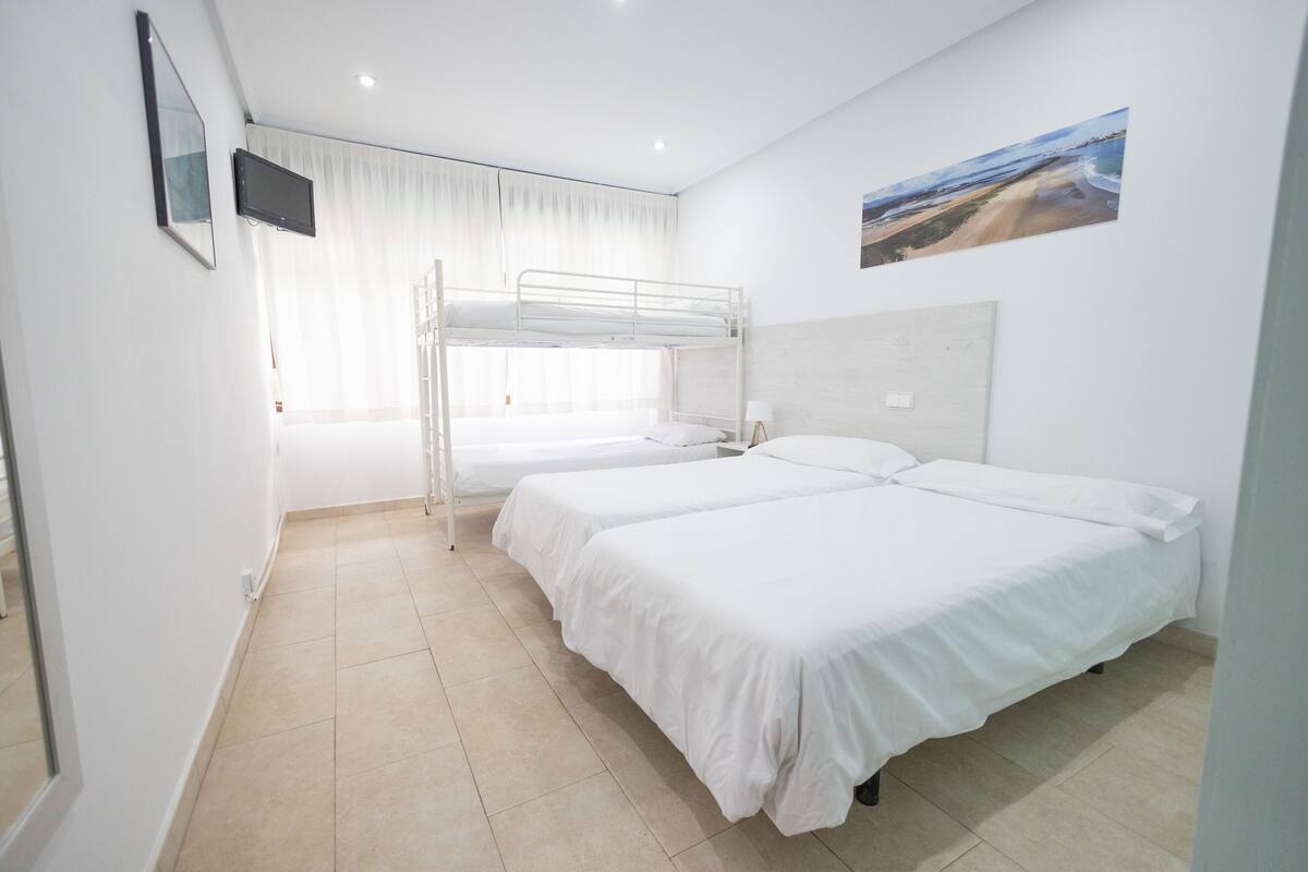 Une chambre avec des lits superposés, un téléviseur à écran plat, une fenêtre avec des rideaux et un tableau représentant une vue sur la plage.