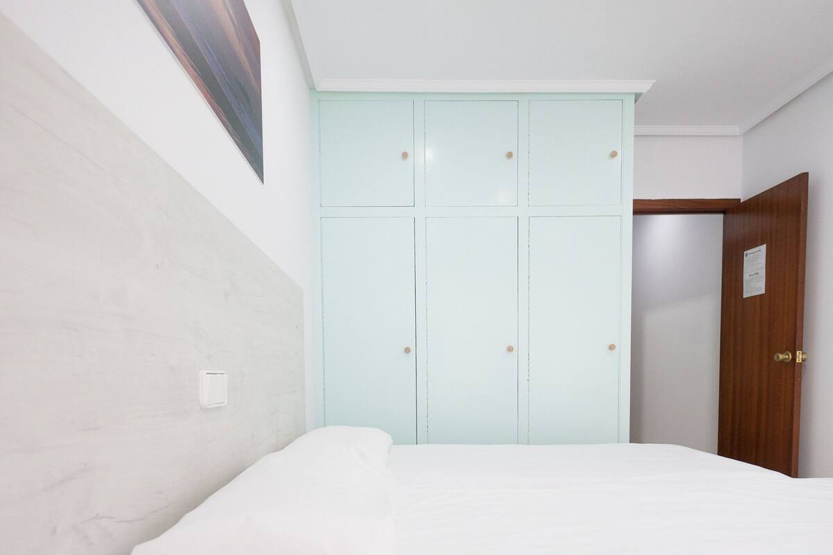 Une chambre à coucher avec un lit, une armoire bleu clair et une porte en bois.