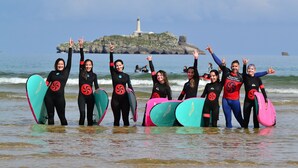 A group of people with surfboards at the beach, with a lighthouse in the background.