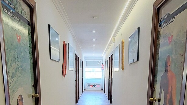 A hotel corridor with wooden flooring, framed pictures on the walls, and doors with glass panels.