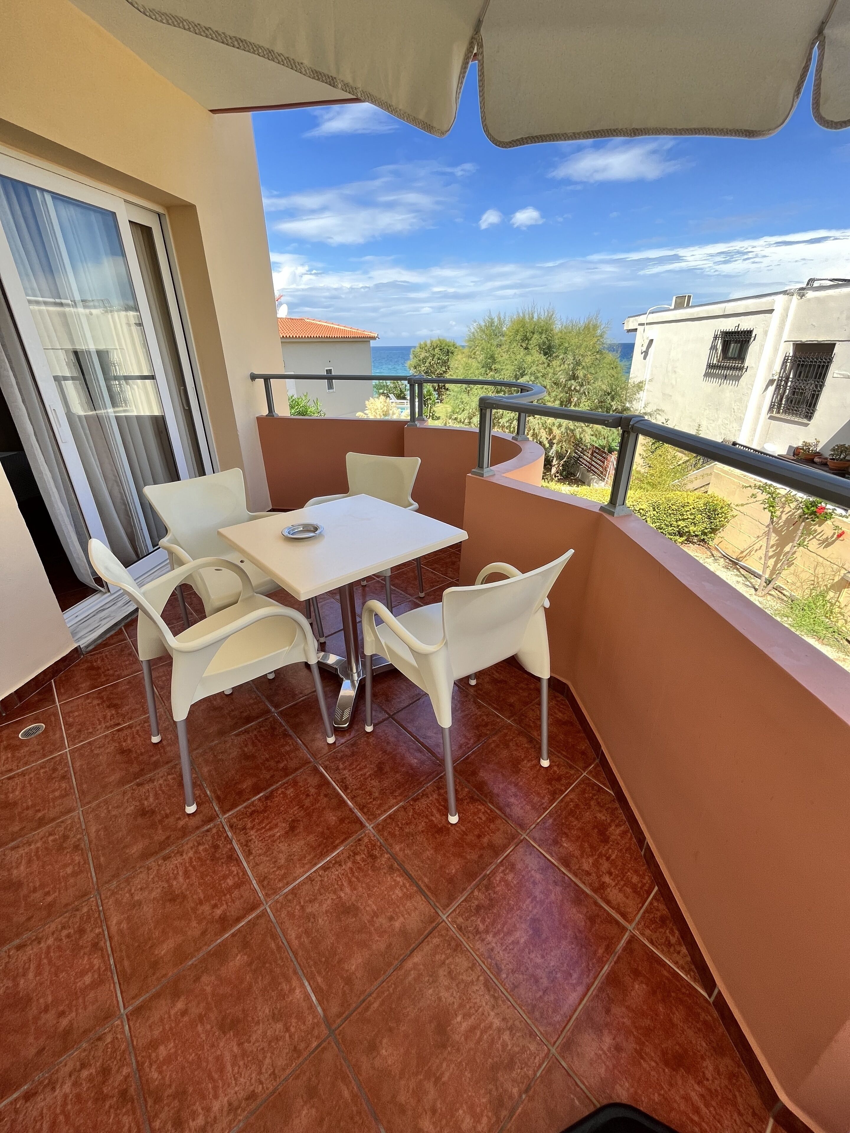 A balcony with a table and chairs, a view of the sea, and a building in the background.