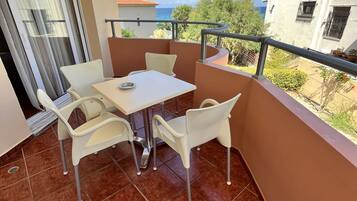 A balcony with a table and chairs, a view of the sea, and a building in the background.