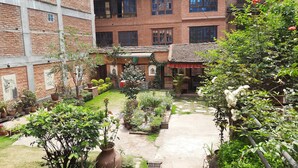 Une cour intérieure agrémentée de plantes en pot, un chemin de pierre et un bâtiment en briques doté de nombreuses fenêtres et de balcons.