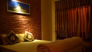 Une chambre d’hôtel avec un mur en briques, un lit avec une couverture enroulée, deux oreillers, une chaise et un tableau représentant un phare.