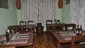 Un espace repas avec des tables et des chaises en bois, un grand vase et des bouteilles posées sur les tables.