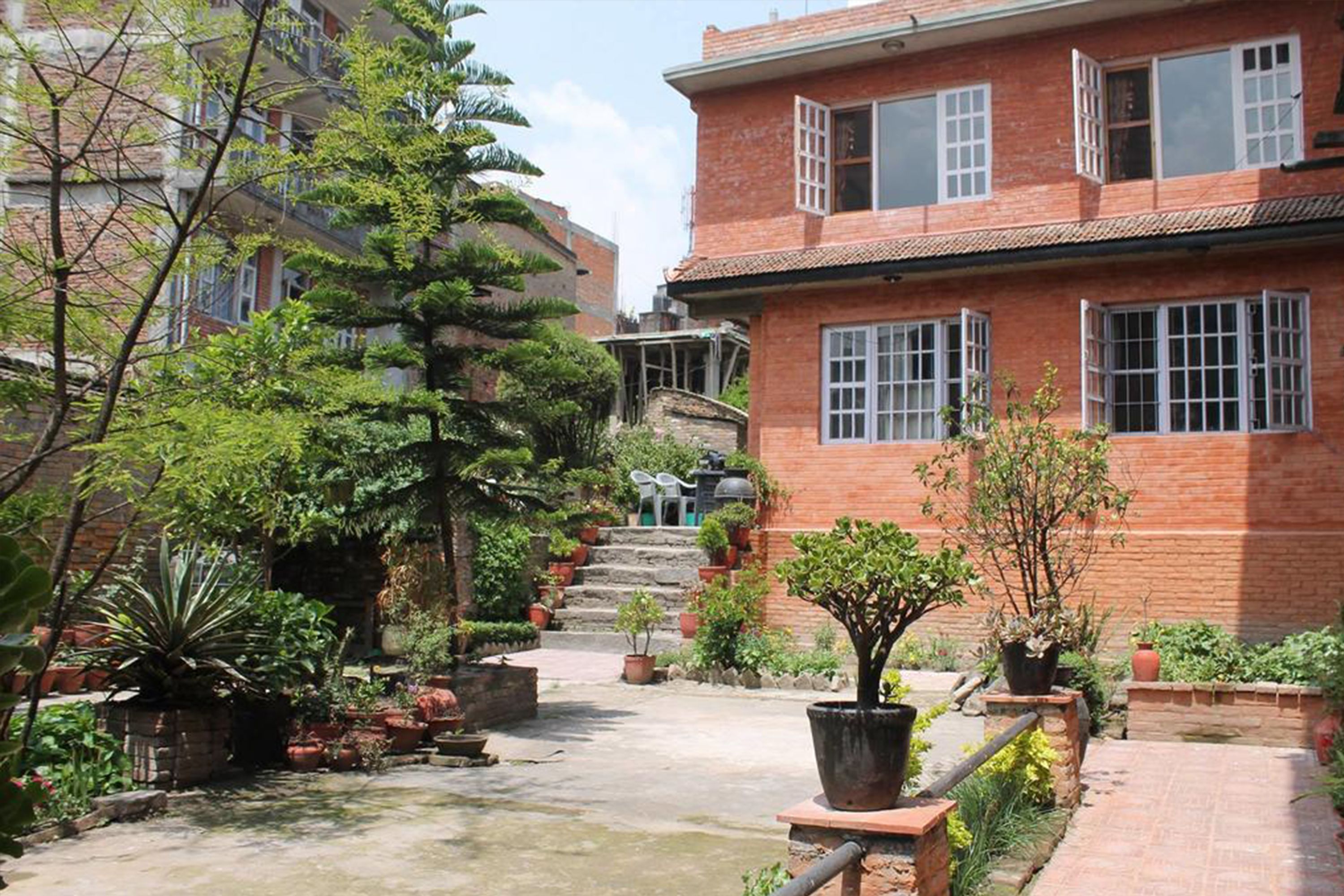 A courtyard with a brick building, potted plants, and a staircase leading to an upper level.