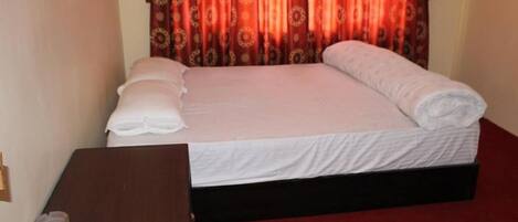 A neatly made bed with white linens and a red curtain backdrop.