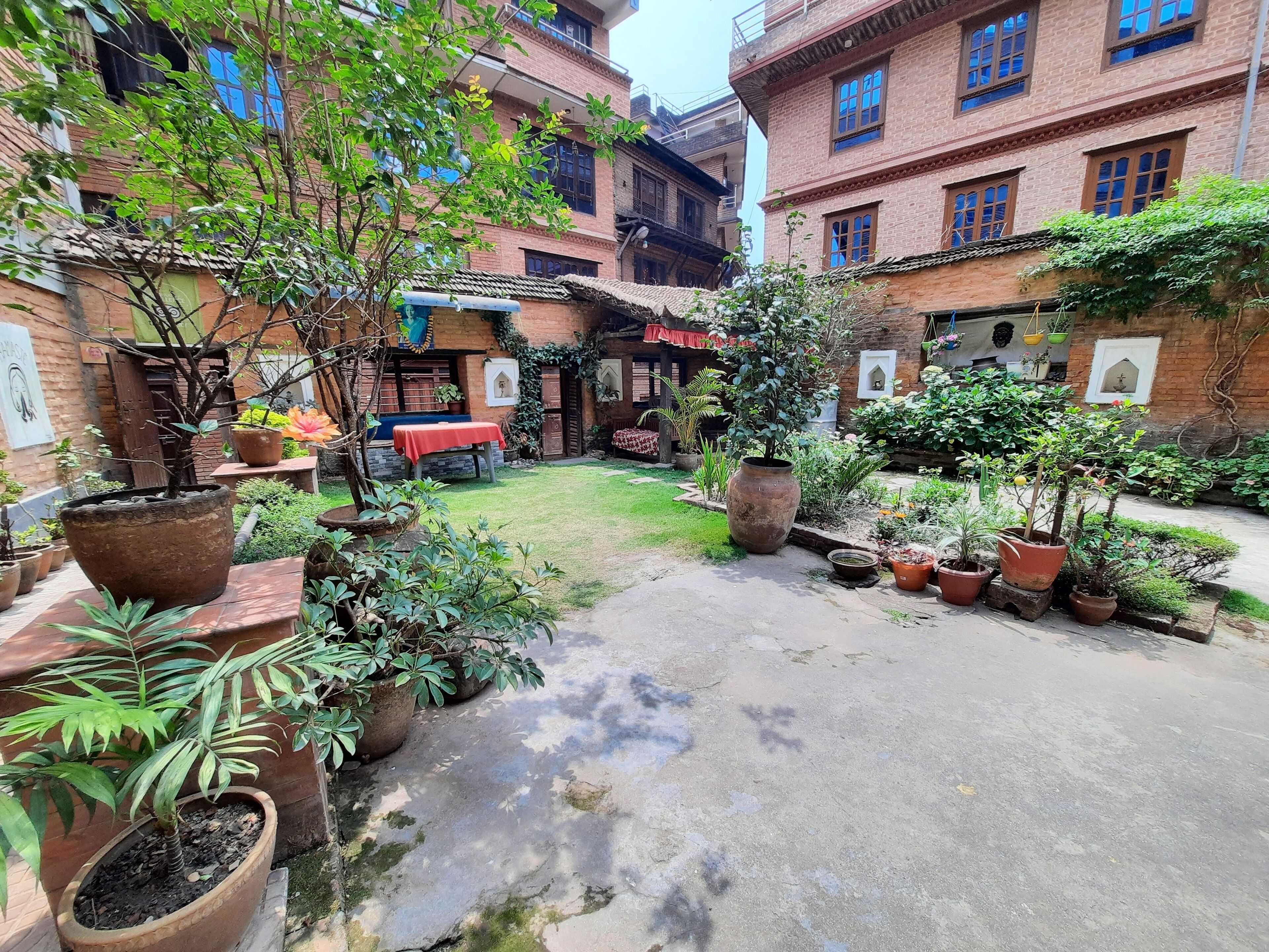A courtyard with potted plants, a red table, and a brick building with multiple windows.