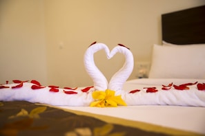A bed with a heart-shaped towel arrangement and a yellow bow, surrounded by red rose petals. - Starling River Resort (Haliyal)