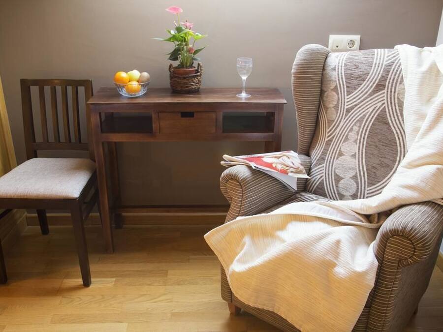 A cozy room with a wooden desk, a comfortable chair, a small table with a basket of oranges, a glass of water, and a potted plant.