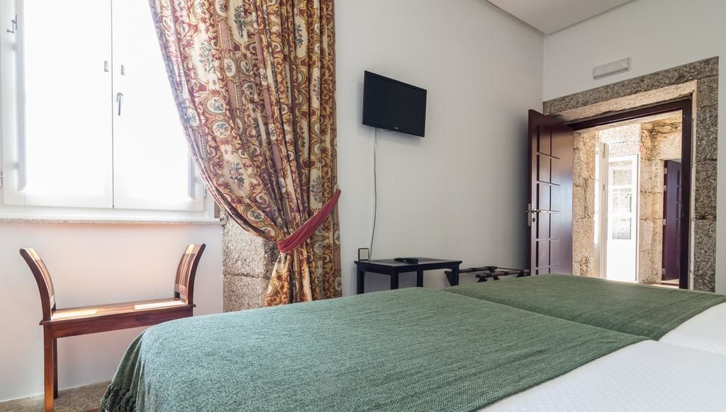 Ein Hotelzimmer mit Bett, Schreibtisch, Stuhl, Fernseher und einem Fenster mit Vorhängen.
