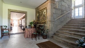 A grand staircase leading to a second floor, a fireplace with a large painting, and a dining area with a table and chairs. - Pazo de Sedor (Arzua)