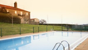 A swimming pool with a metal ladder, surrounded by a fence and a stone building in the background. - Pazo de Sedor (Arzua)