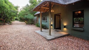 Un edificio con techo de paja, camino de grava y pérgola de madera.