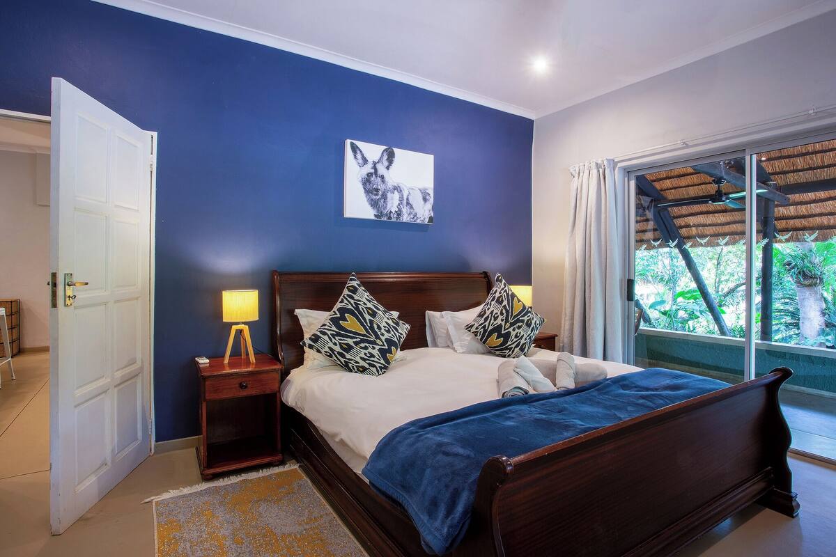 A bedroom with a bed, bedside tables, a lamp, a painting, and a window with a view.