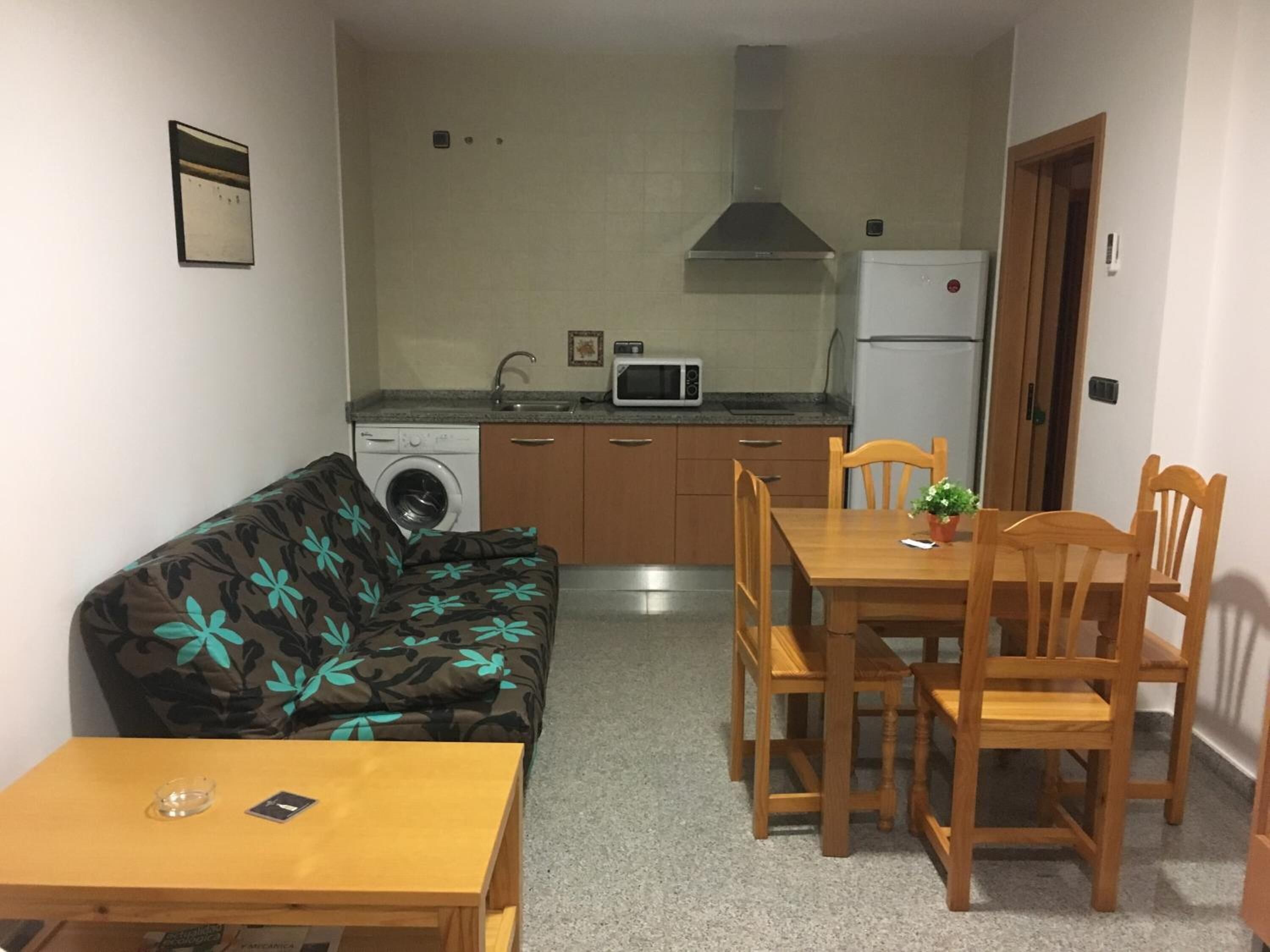 A compact living space with a kitchenette, a dining area with wooden furniture, and a sofa with a floral pattern.
