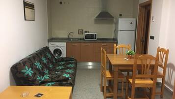 A compact living space with a kitchenette, a dining area with wooden furniture, and a sofa with a floral pattern.