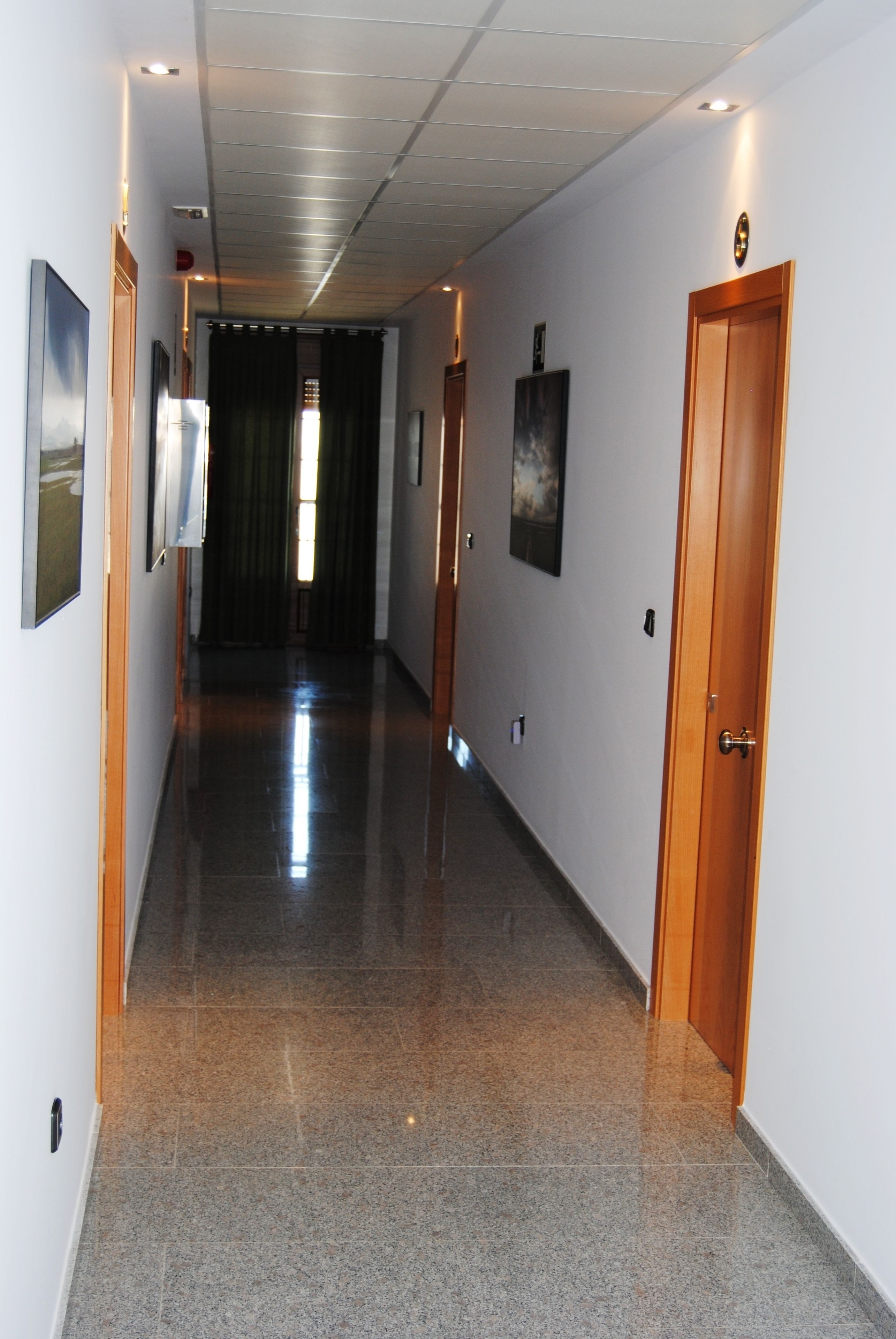 A corridor with a polished floor, framed artwork on the walls, and a wooden door at the end.