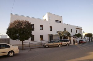 Un edificio moderno con un letrero que dice "HOTEL" en la fachada. Varias coches estacionados en la parte delantera, y un árbol a la izquierda.