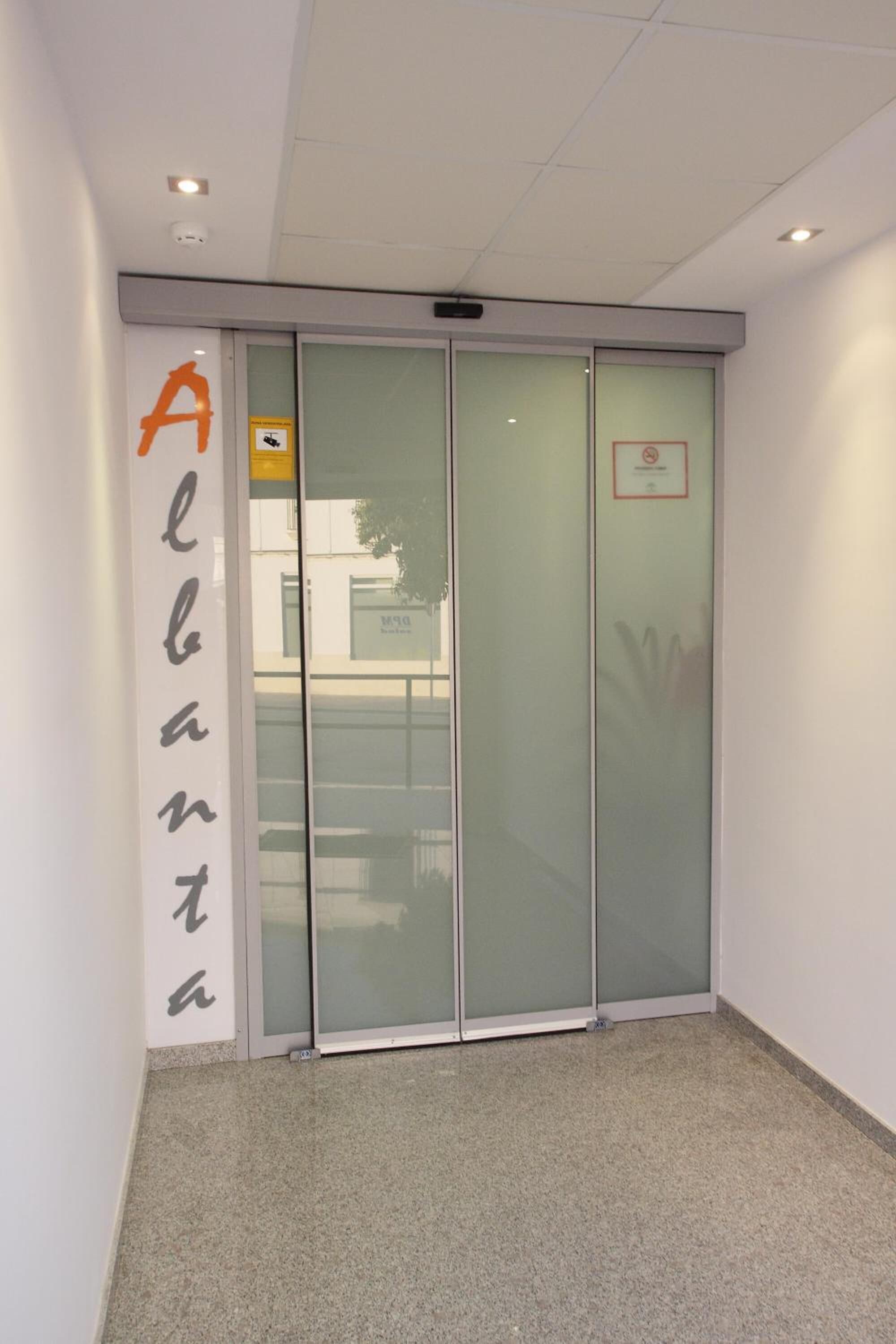 Un pasillo con una puerta de vidrio esmerilado, un letrero con la palabra "Alberta" en la pared y un cartel de "No fumar" en la puerta.